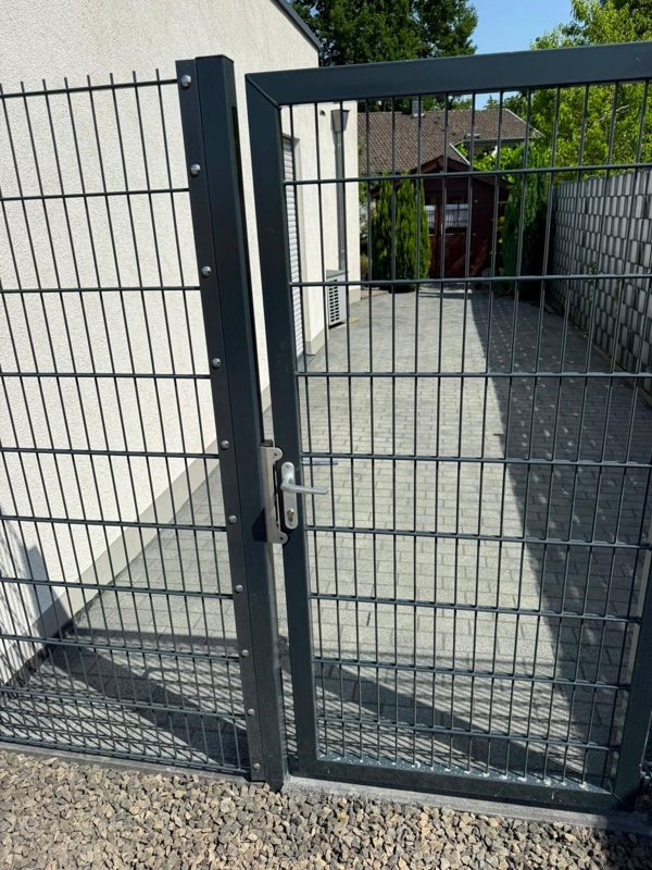 Anthrazitfarbener Doppelstabzaun mit Gartentür vor gepflasterter Fläche